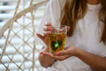 Glas CBD vruchtenthee in de hand, met het theezakje in het glas